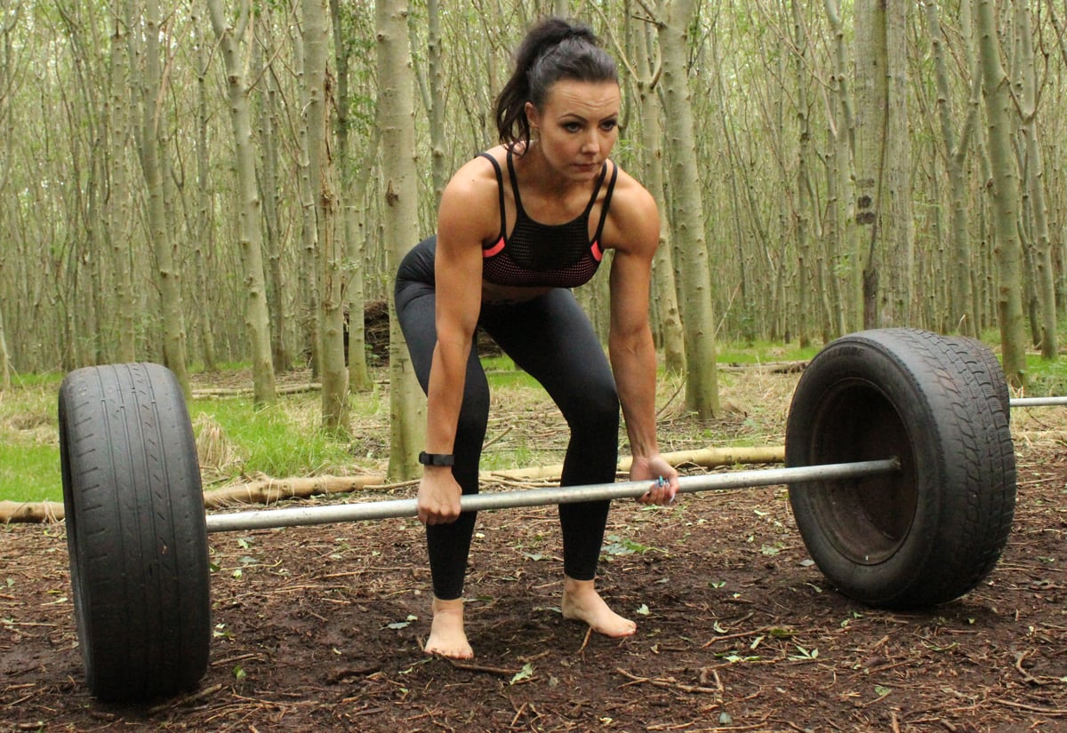 Coach Aga lifting a dumbbell made out of tires in the forrest